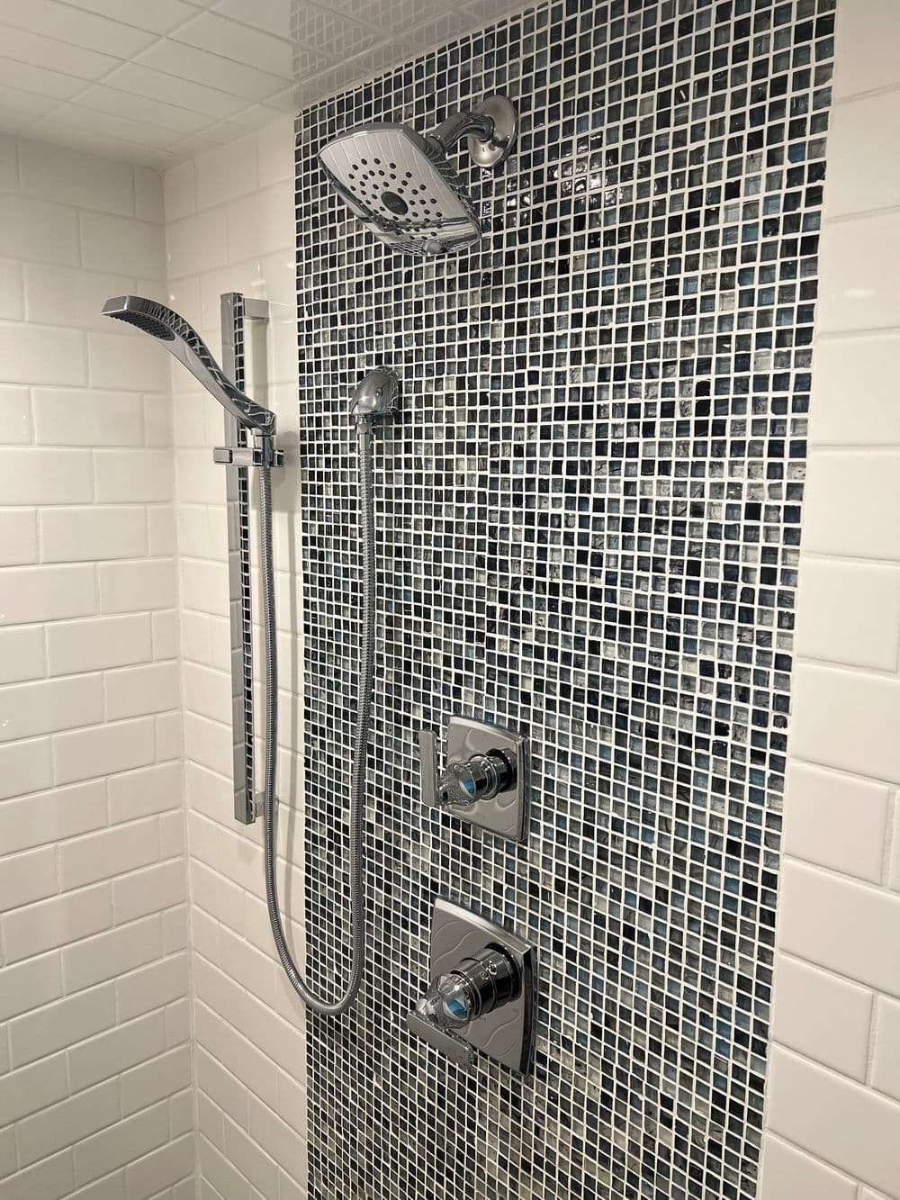 Modern shower with sleek chrome fixtures and black and white tile backsplash.