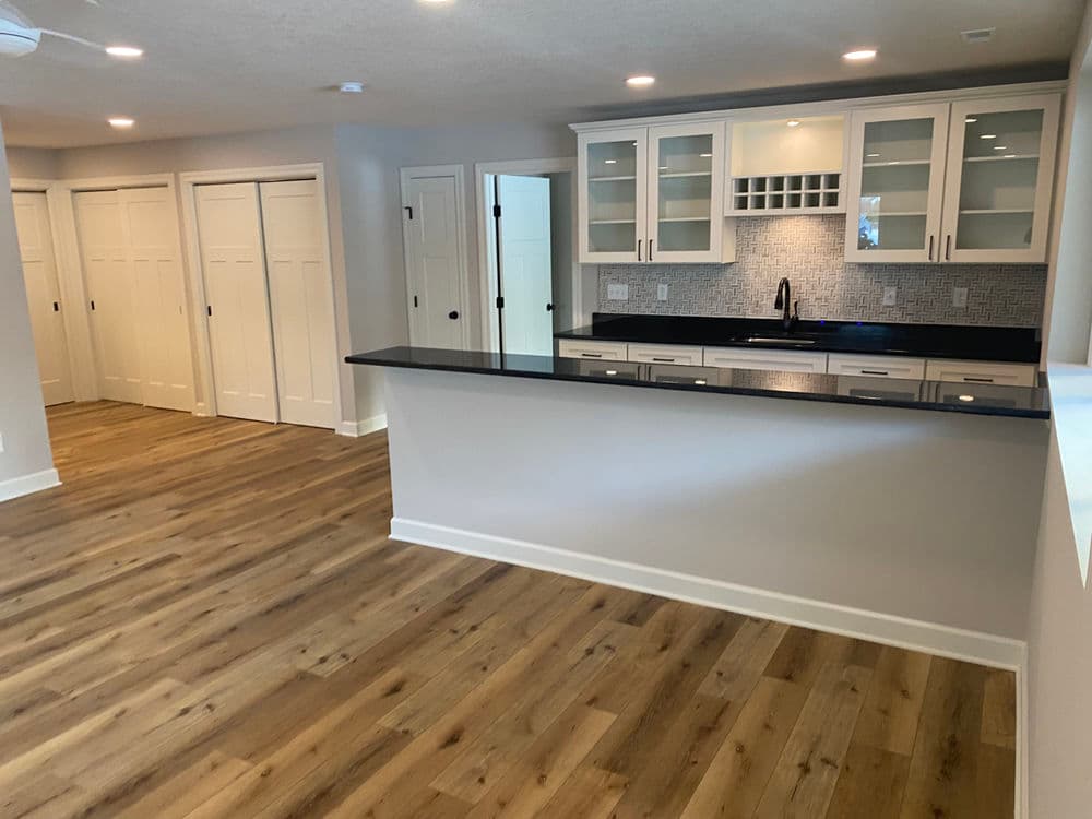 Modern kitchen with white cabinets, black countertop, and open living space with hardwood floors.