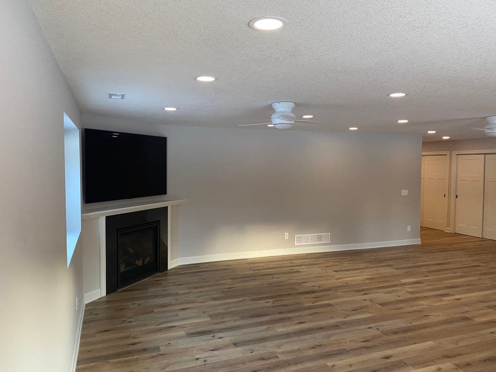 Modern living room with hardwood floors, fireplace, ceiling fans, and wall-mounted TV.