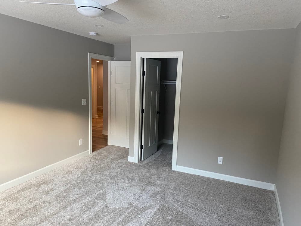 Newly renovated bedroom with gray walls, light carpet, and open doorways. Bright and spacious design.