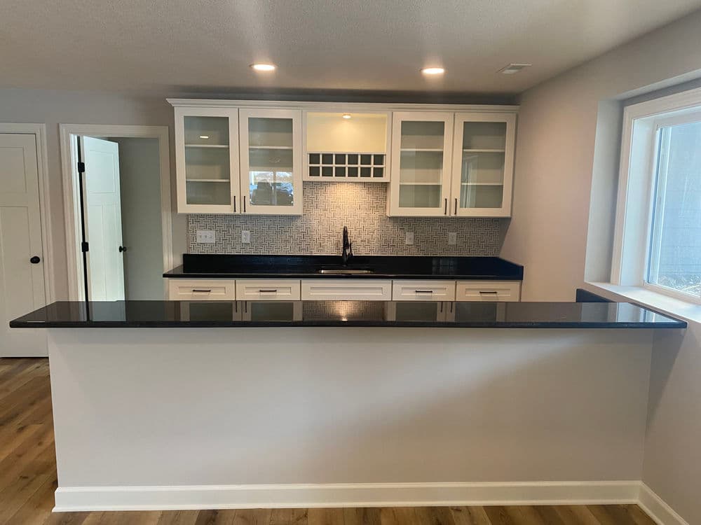 Modern kitchen with black granite countertop, white cabinets, and glass tile backsplash.