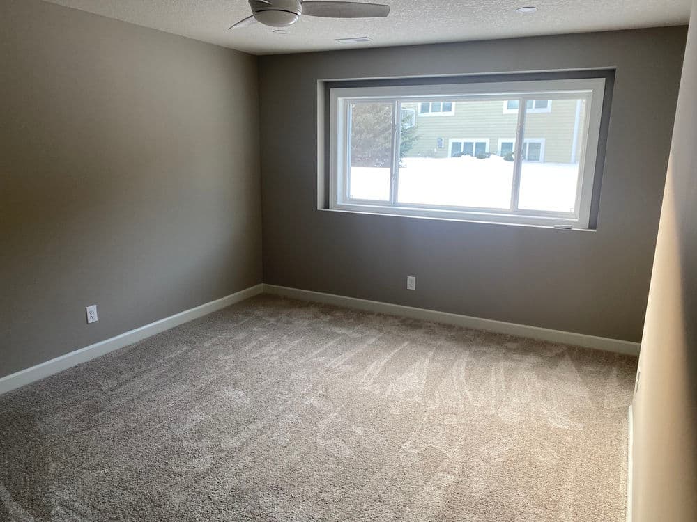 Empty room with fresh carpet and large window, showing bright natural light and neutral walls.