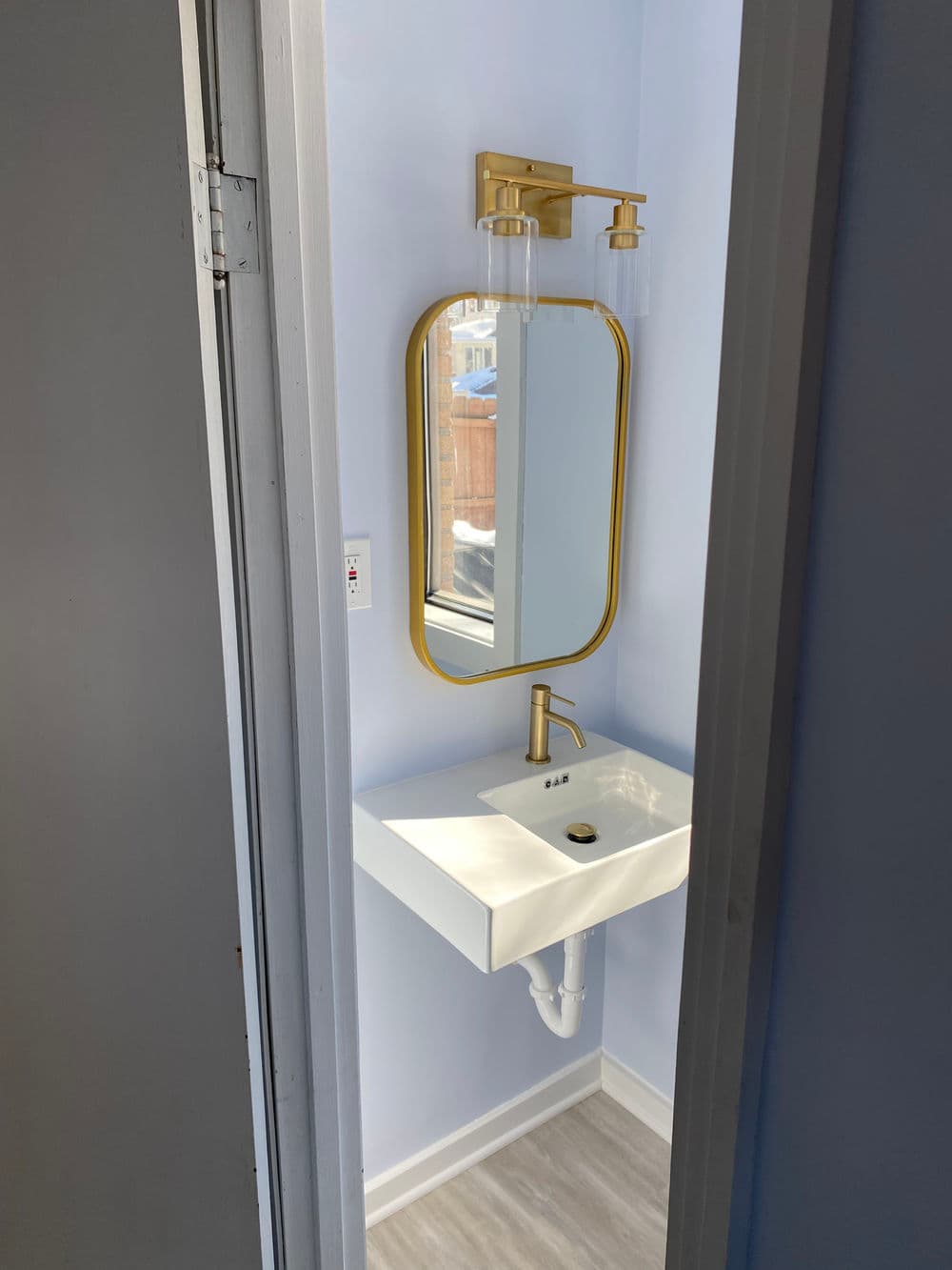 Modern bathroom featuring gold-accented mirror and faucet, minimalistic sink, and light blue walls.