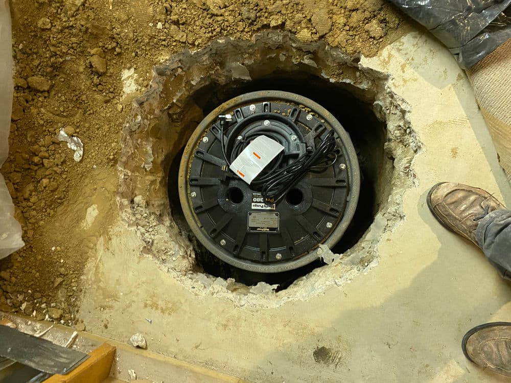 Sump pump installation in a concrete pit, showing wiring and surrounding soil.