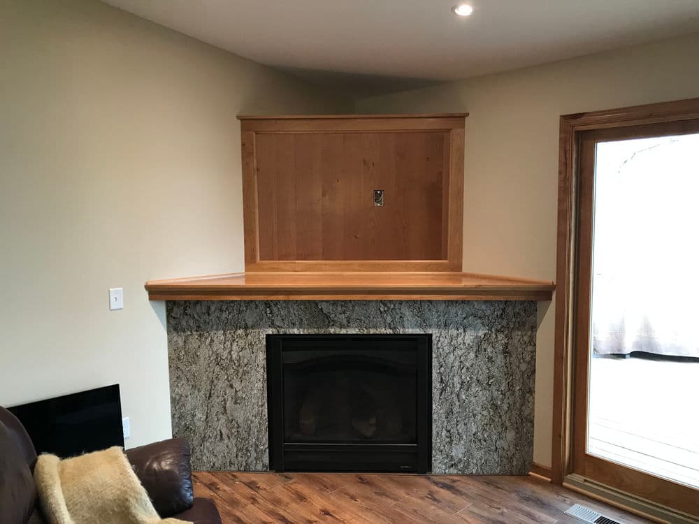 Modern living room with a granite fireplace, wooden mantle, and large windows for natural light.