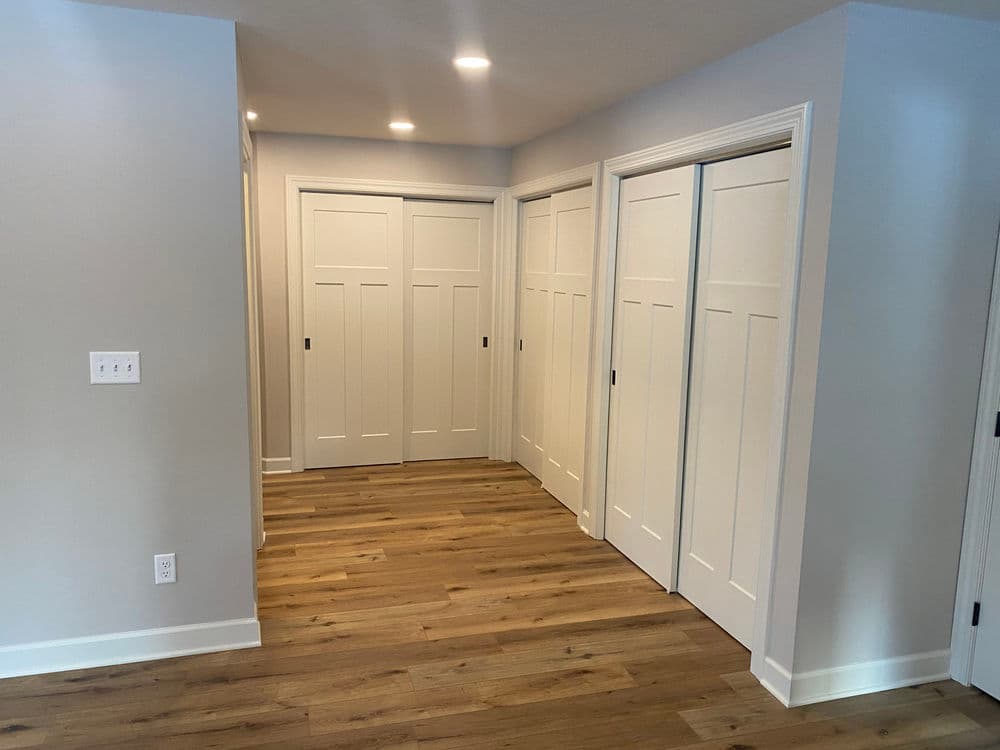 Modern hallway with sliding white panel doors and hardwood flooring, brightened by recessed lighting.