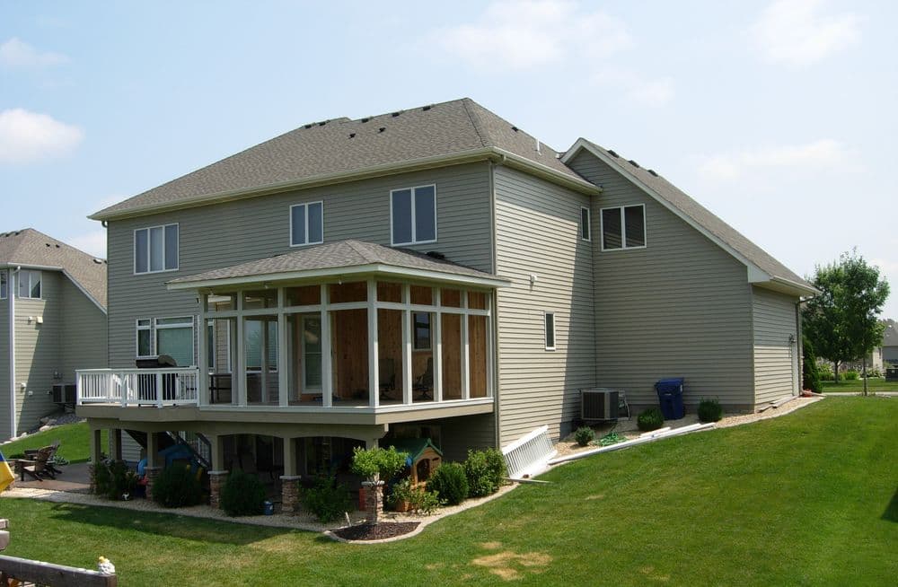 Modern two-story house with a screened porch and landscaped yard. Bright, sunny day.