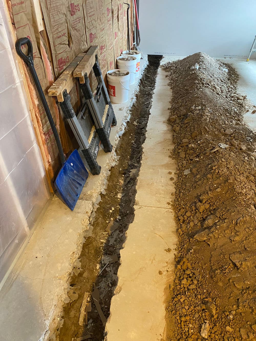 Excavated trench in a basement with tools and materials for plumbing installation.