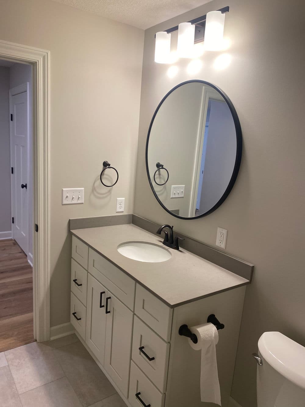 Modern bathroom with circular mirror, sleek countertop, and stylish lighting fixtures.