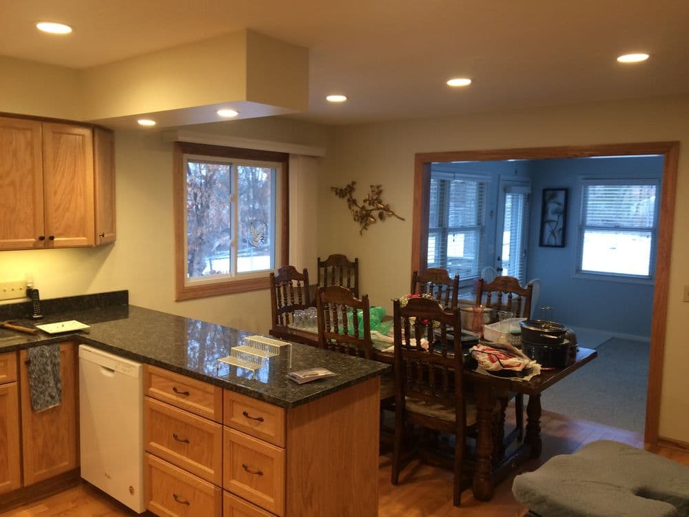 Modern kitchen with wooden cabinetry, granite countertops, and a dining area featuring a table and chairs.