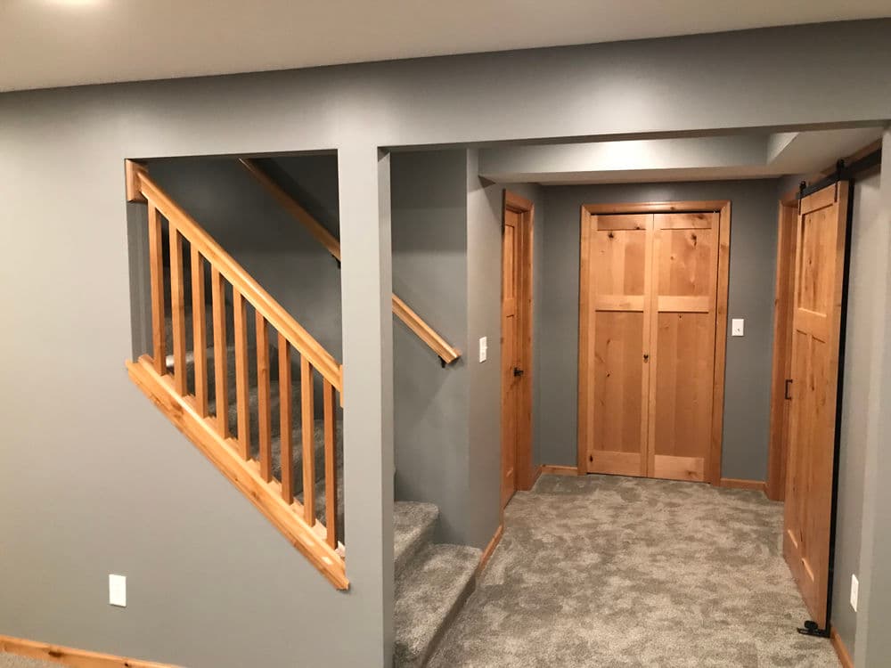 Modern basement interior with gray walls, wooden staircase, and two wooden doors.