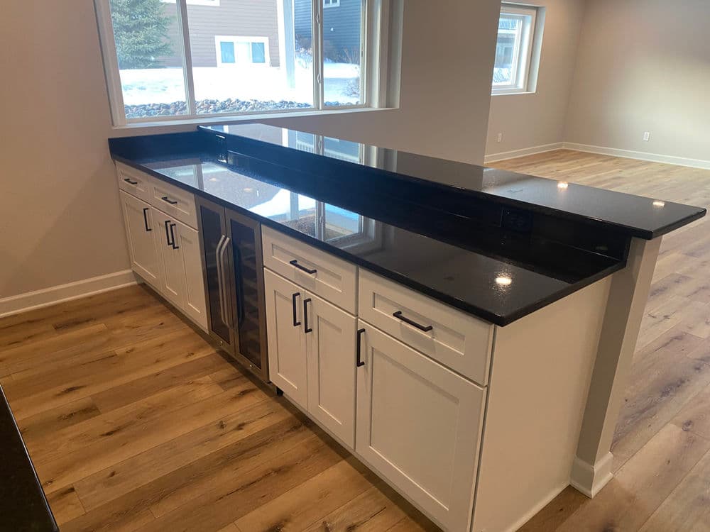 Modern kitchen featuring a black granite countertop, white cabinets, and a large window.