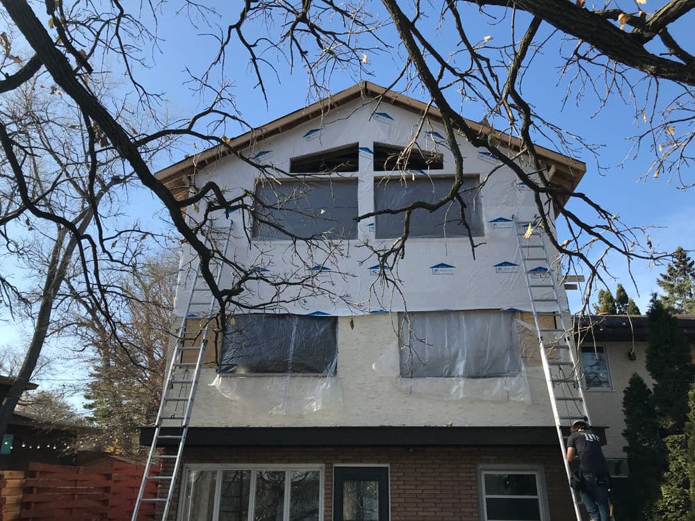 Home exterior renovation with scaffolding, featuring construction materials and clear blue sky.