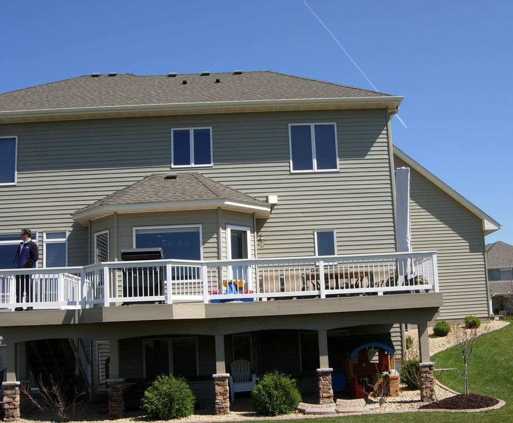 Two-story modern home with a spacious deck and sliding glass doors on a sunny day.