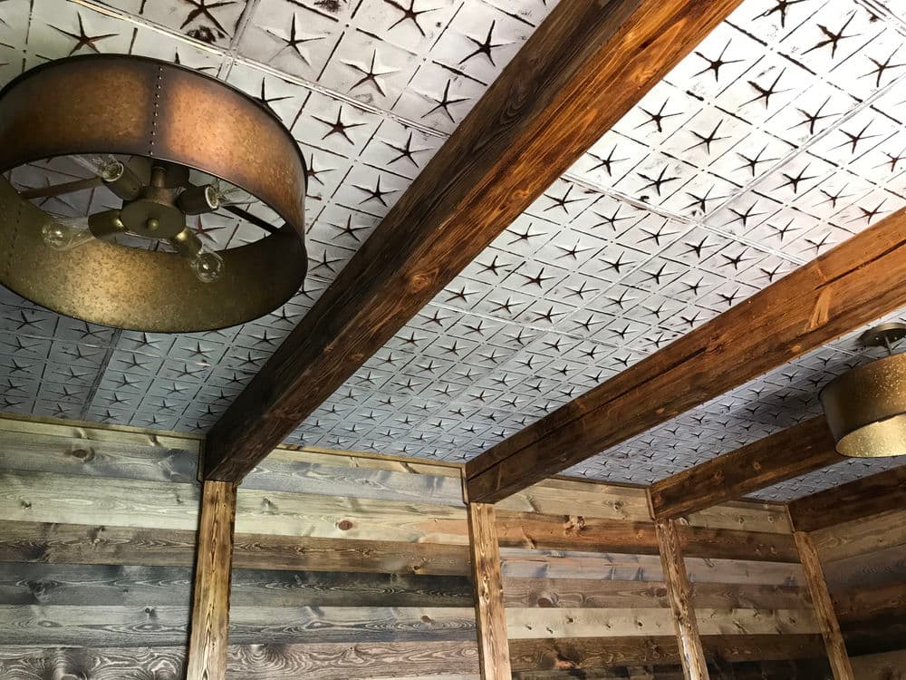 Rustic interior with wood beams, star-patterned ceiling tiles, and vintage light fixtures.