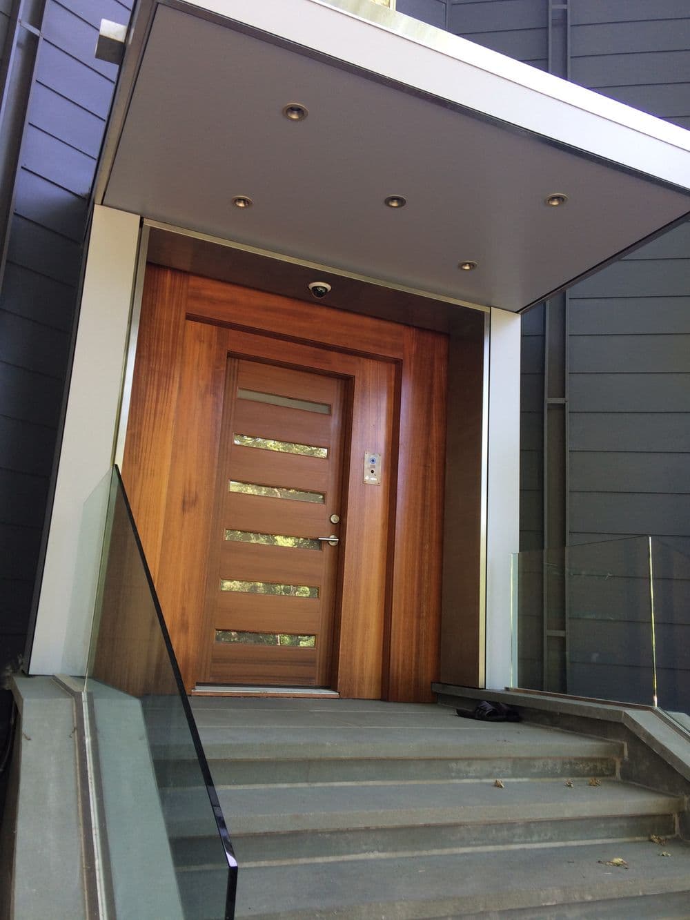 Modern wooden door with decorative paneling, sleek entryway, and glass railing.