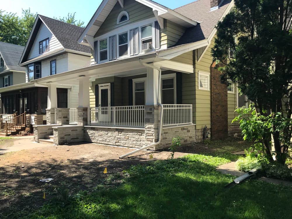 Modern green house with porch, stone accents, and landscaped yard. Ideal for family living.