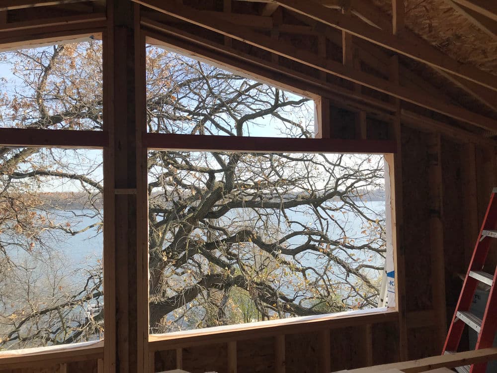 New construction interior with large windows showcasing a view of trees and water.