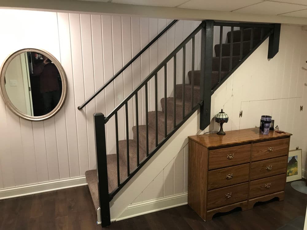 Staircase leading to upper level with round mirror and wooden dresser in basement setting.