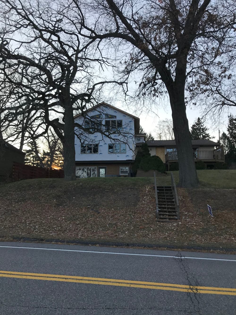 Two-story house on a hillside with large windows and trees, captured at sunset.