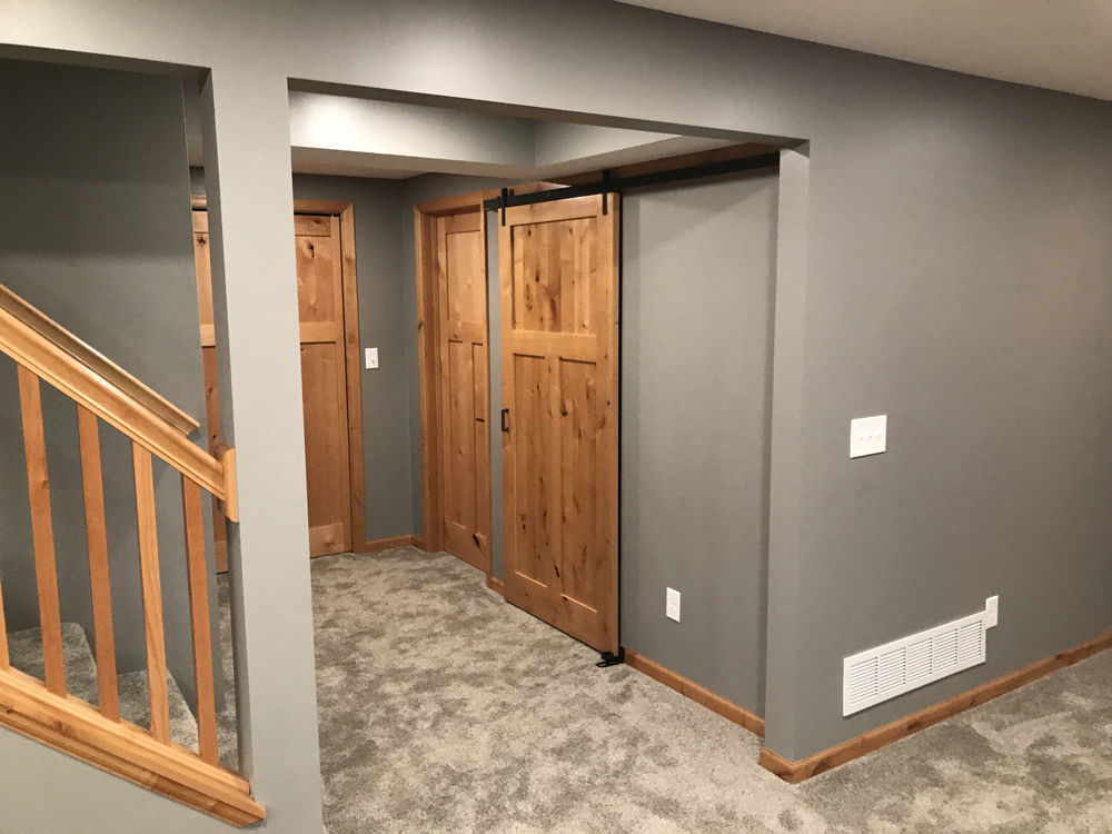 Modern hallway featuring gray walls, wooden doors, and carpet flooring with staircase.