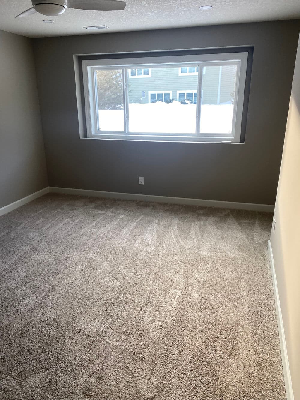 Empty room with carpeted floor, large window, and light gray walls, featuring natural light.