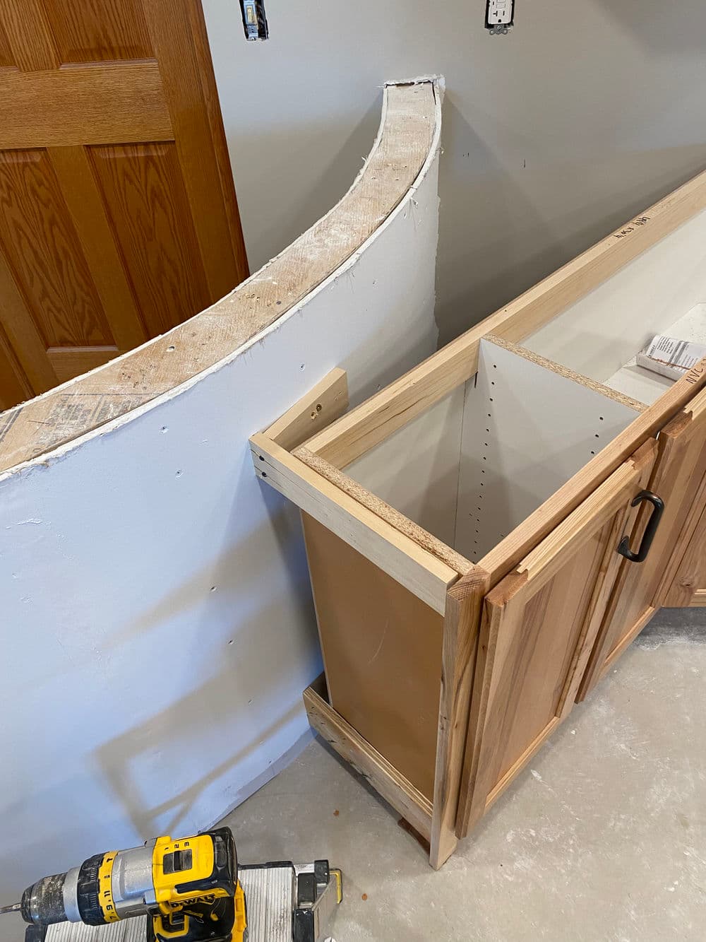 Curved kitchen drywall and unfinished wooden cabinet during home renovation project.