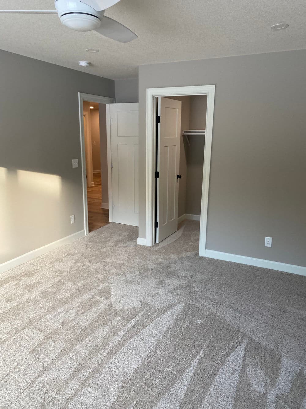 Spacious bedroom with carpet, ceiling fan, and adjacent closet door in modern design.