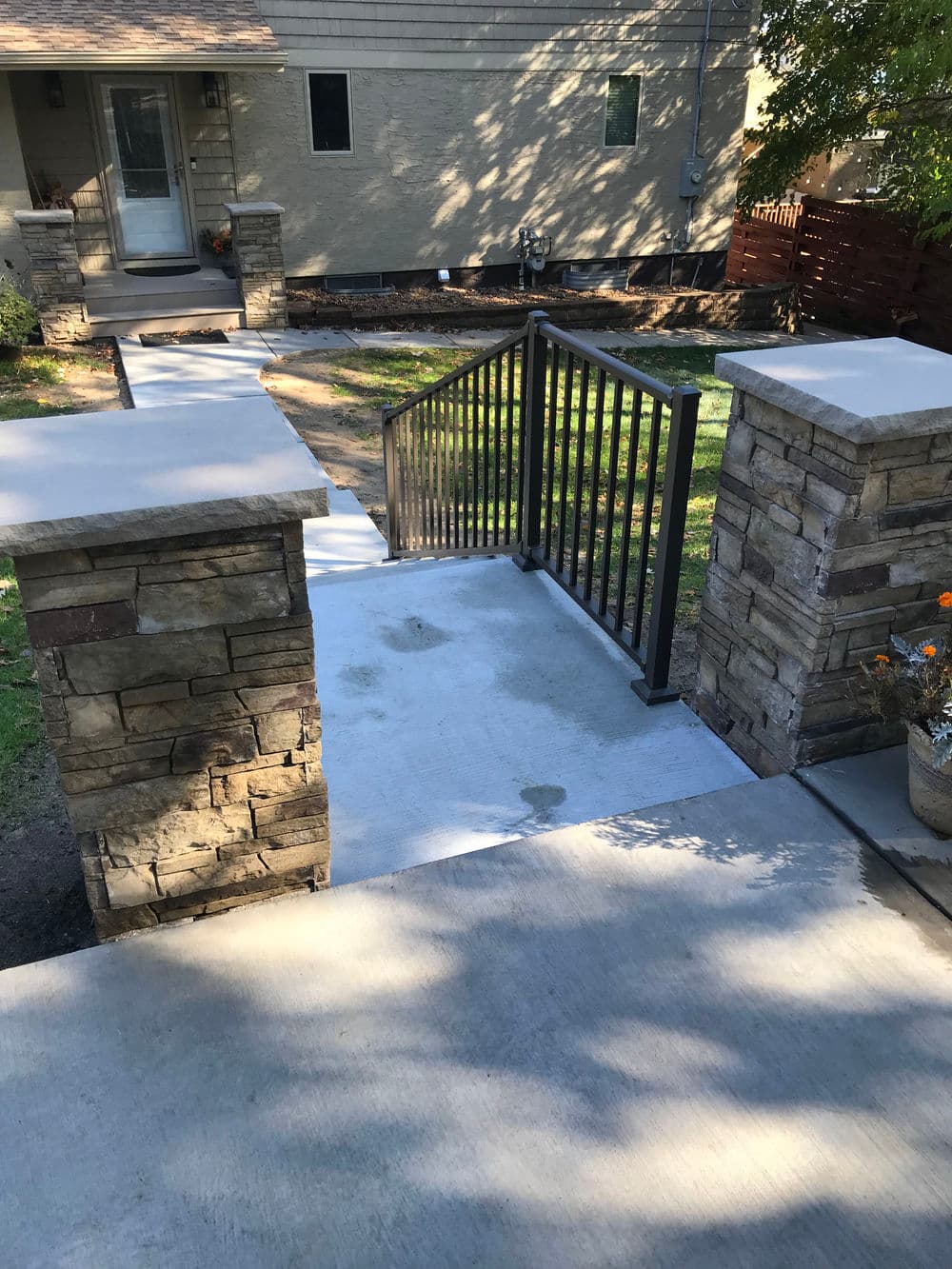 Concrete ramp with stone pillars and metal railing leading to a house entrance.